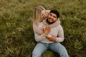 A couple laughing together while sitting in tall grass during golden hour.