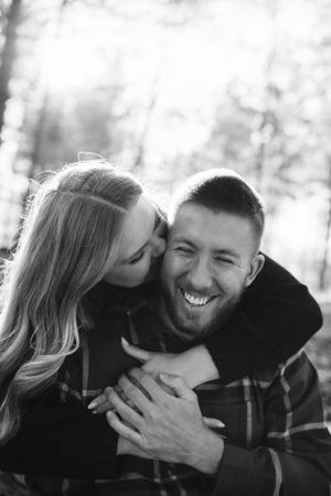 A romantic black and white portrait of a couple embracing and laughing in the woods.