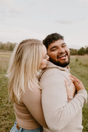 A couple sharing a warm embrace in a sunny meadow wearing neutral tones.