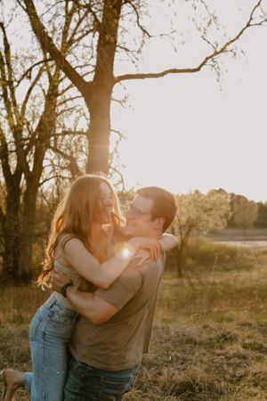 A romantic sunset embrace between a couple in a field with sunlight streaming through trees behind them.