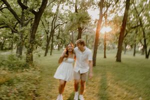 A playful couple walking through a sunlit park wearing matching white outfits.
