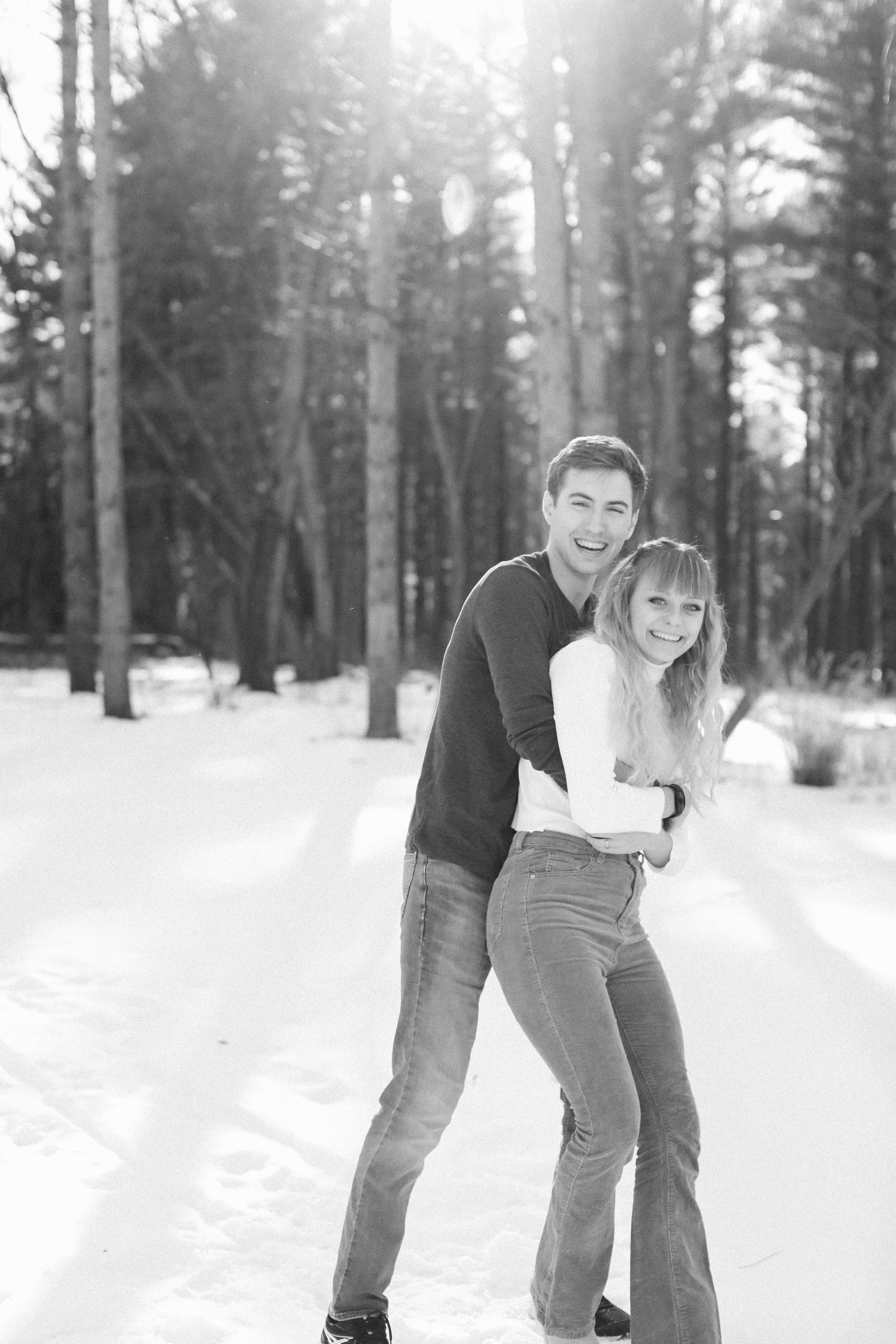 Loving couple embraces while playing in snowy winter forest setting.