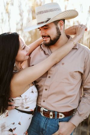 Romantic western-style couple embrace wearing cowboy hat and summer outfits.