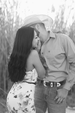 Romantic couple in Western attire share an intimate moment among trees in a black and white portrait.