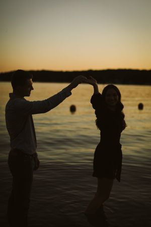 Silhouetted couple dancing by lake at sunset creates romantic scene.