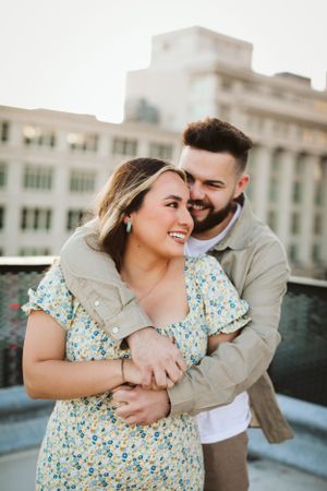 Couple shares joyful embrace on rooftop during golden hour in casual spring outfits.
