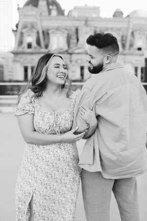 A romantic couple shares a candid laugh together in front of an elegant historic building.
