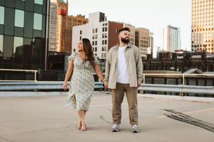 A couple walks together on a rooftop with city buildings in the background.