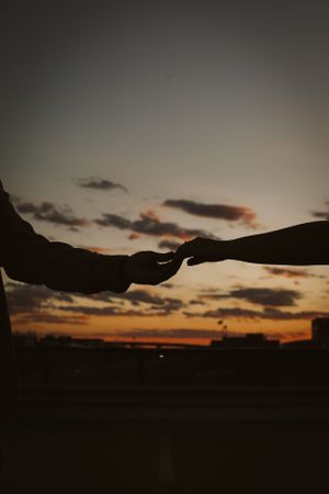Two silhouetted hands reach toward each other against a dramatic sunset sky.