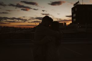 A silhouette of a couple embracing against a sunset urban skyline.