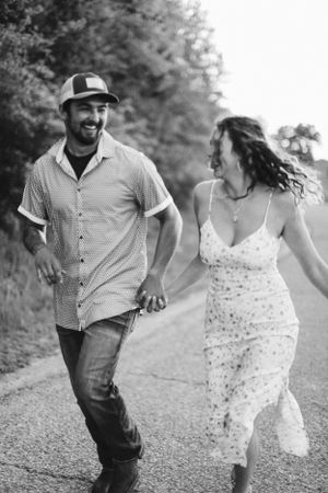 Candid black and white photo of couple running and laughing together on a rural road.