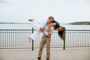 Playful couple strikes fun pose by waterfront railing.