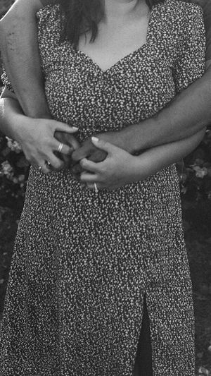 A dress with delicate floral print and hands clasped in an intimate black and white photo.