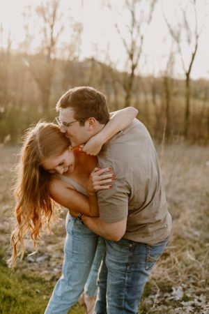 Couple sharing passionate embrace in golden sunset light with natural backdrop.