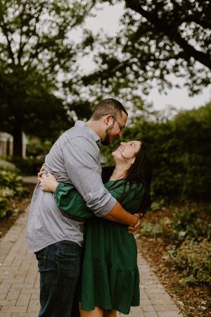 Romantic couple embracing on brick pathway surrounded by trees.
