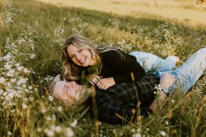 A joyful candid moment between a couple lying in a summer meadow.