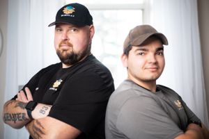 Moving company employees in black uniforms and caps pose together in bright room.