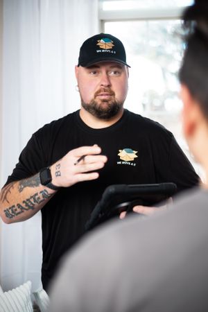 Person in black company uniform gesturing while speaking in office environment.
