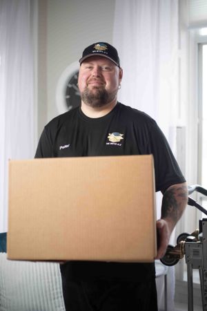 Person in black uniform holding cardboard boxes in bright office setting.