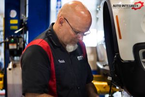 Auto technicians in red and black uniforms working in professional repair facility.