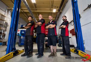 Team of mechanics standing in formation at modern auto repair facility.