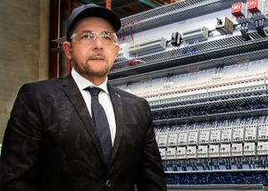 Business professionals in suits examining manufacturing equipment in factory setting.