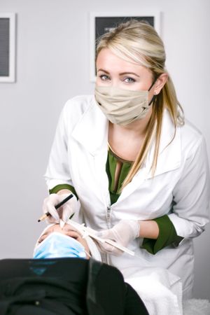 Healthcare worker wearing protective equipment performing dental examination in clinical setting.