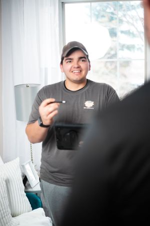 Moving company worker in gray uniform and cap stands in sunlit room.