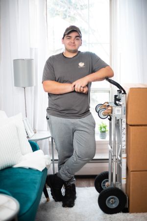 Moving company worker in gray shirt demonstrates professional equipment in bright indoor setting.