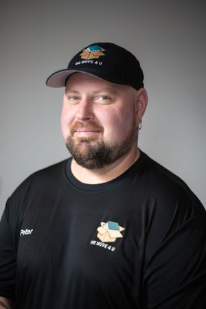 Person in black t-shirt and baseball cap with company logo against gray background.