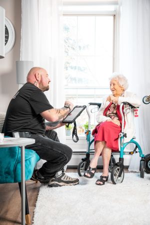 Moving professionals assist elderly customer with equipment in bright living room.
