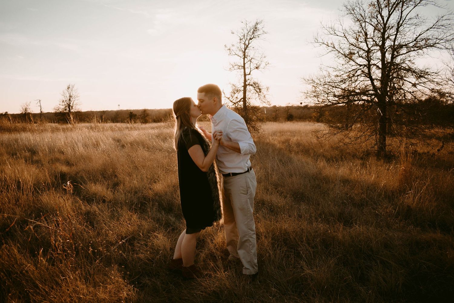 Intimate portrait of a couple standing close together in a rustic field at sunset.