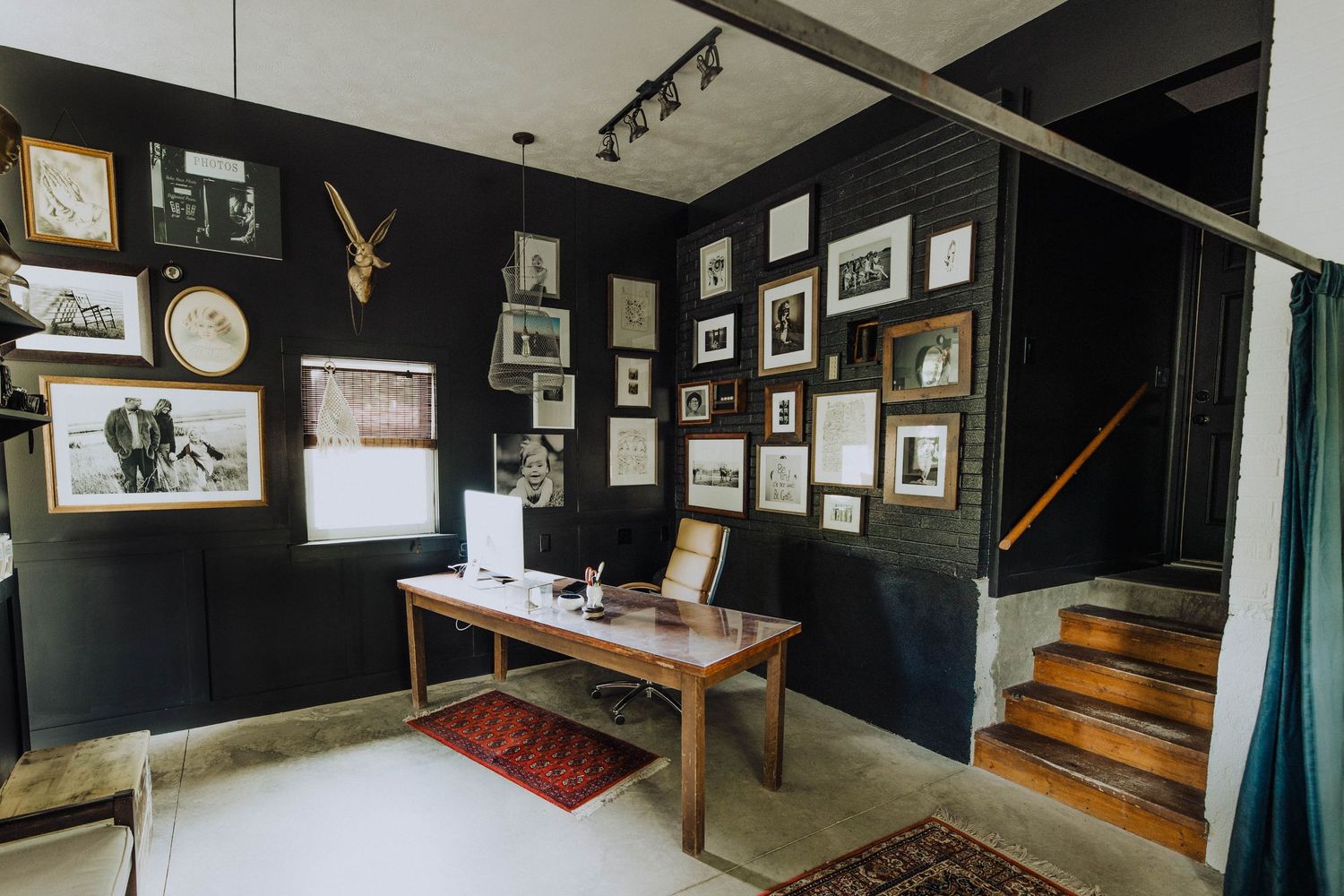 Home office space with dark walls decorated with framed photos and wooden staircase.