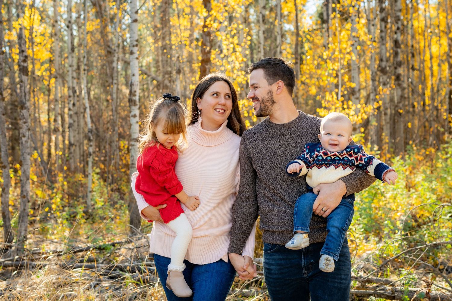 Family of four enjoying a sunny autumn day in a forest with golden yellow leaves.