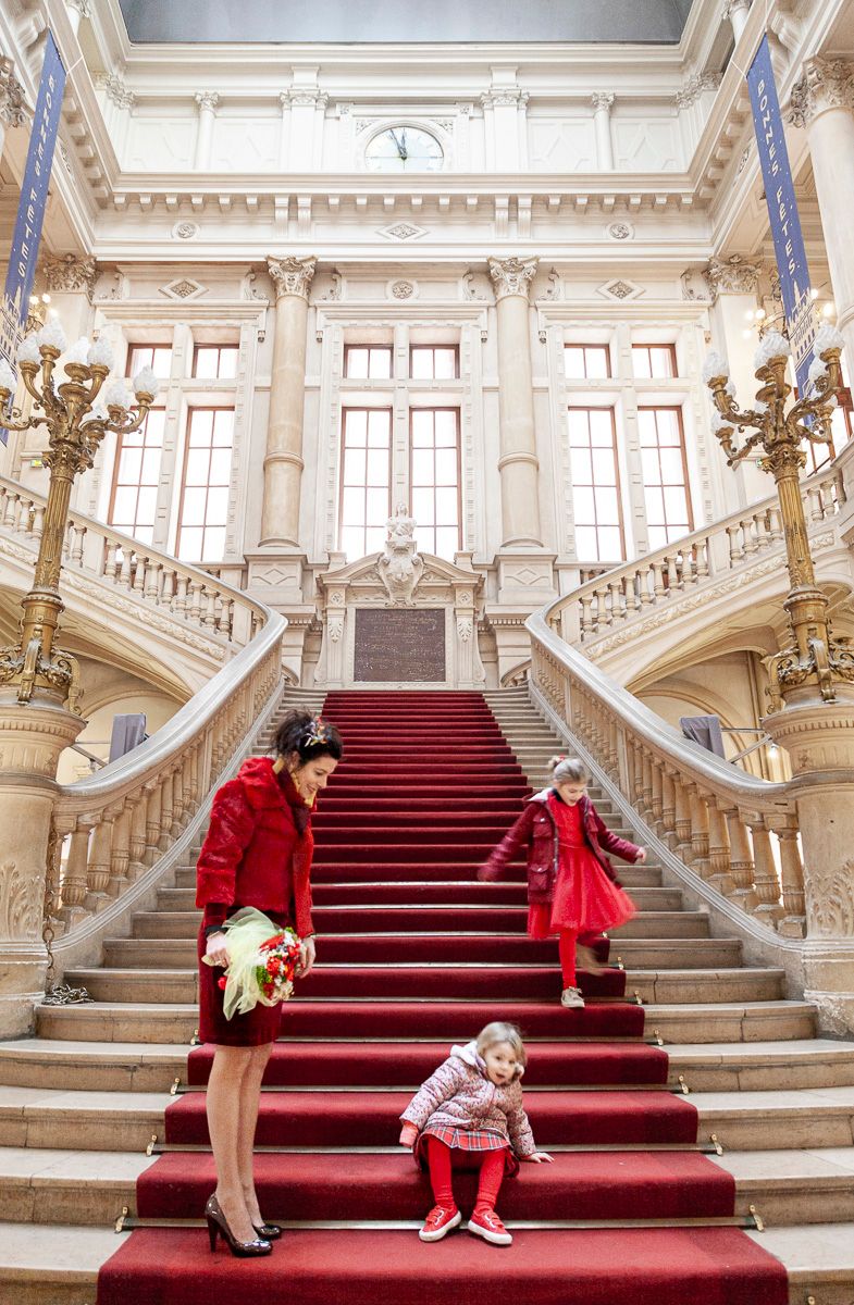 Grand staircase with red carpet featuring people in red and white outfits ascending marble steps.