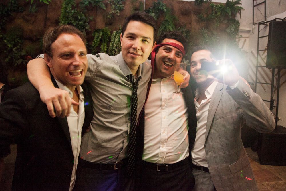 Three friends smiling and posing together at a party with camera flash in the background.