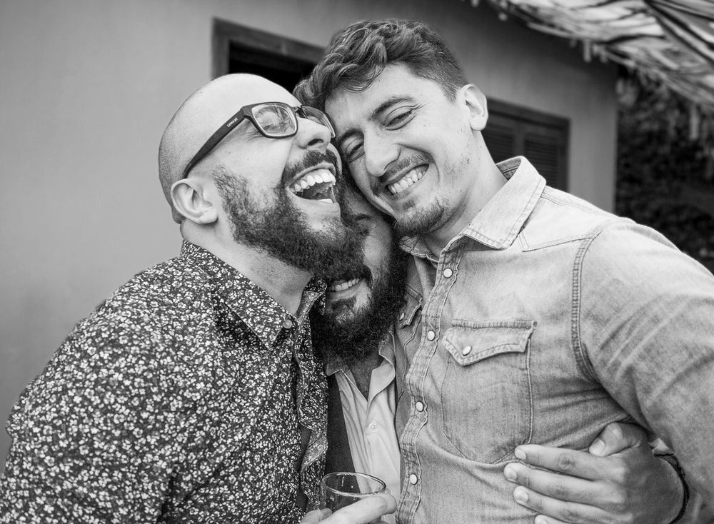 Two friends sharing a laugh in black and white, one with a beard wearing glasses.