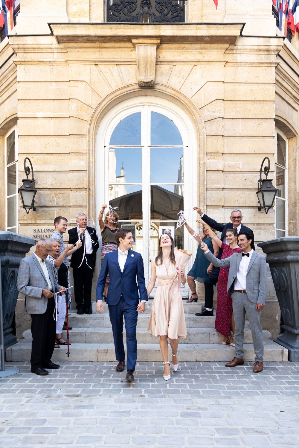 Wedding celebration outside historic French building as guests throw confetti.