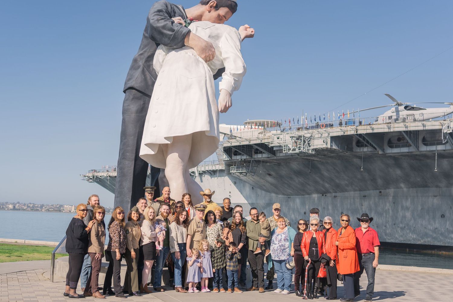 Large group stands beneath the iconic Unconditional Surrender statue at the USS Midway Museum in San Diego.