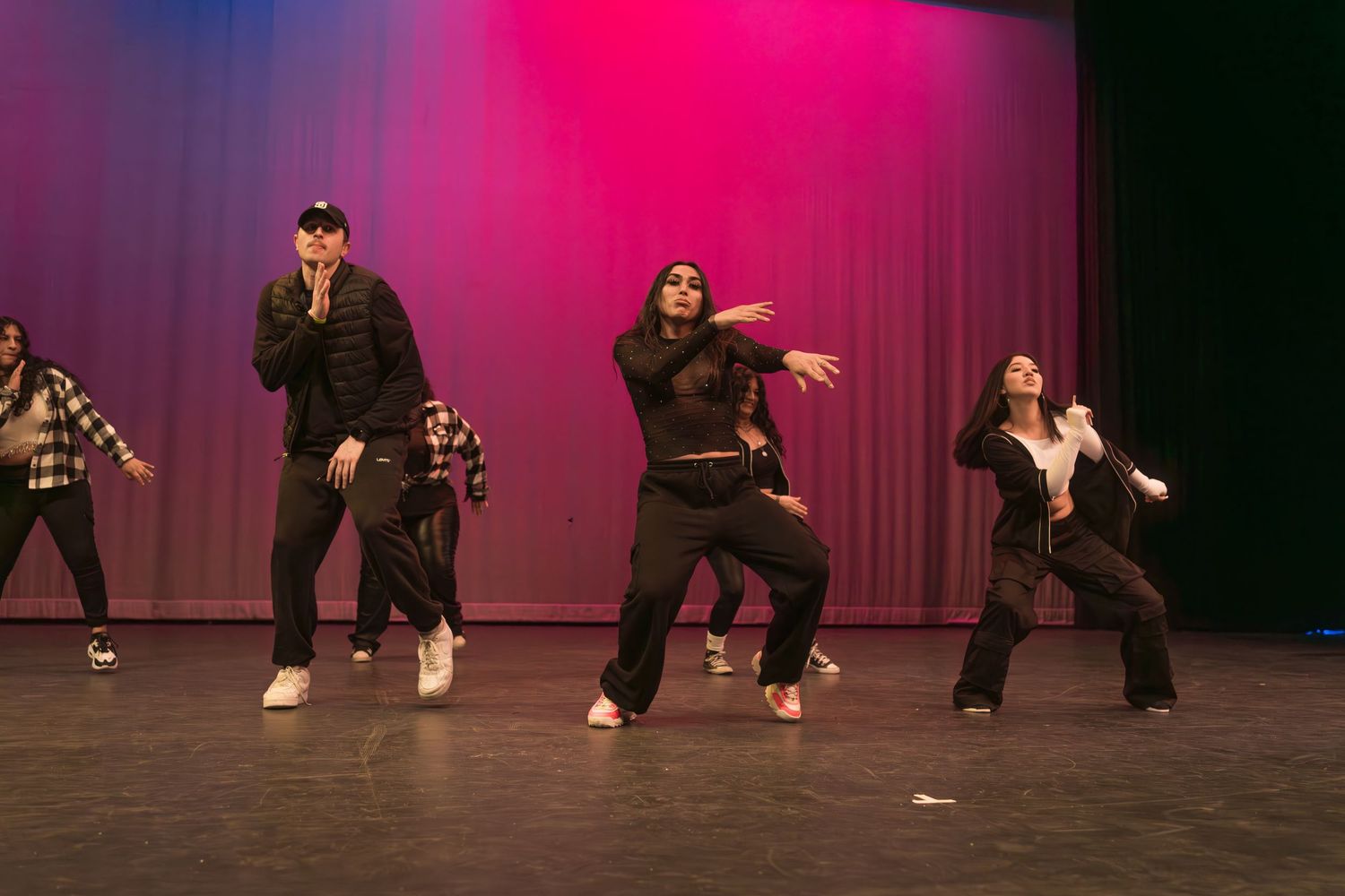 Dancers perform a hip hop routine on stage with dramatic pink and purple lighting effects in the background.