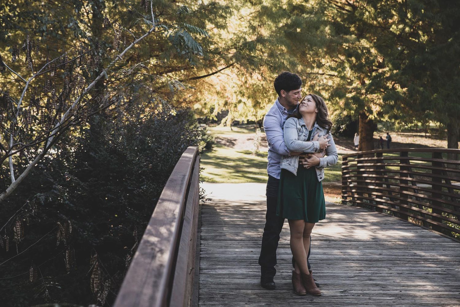 Couple sharing intimate moment on wooden bridge in autumn park setting.