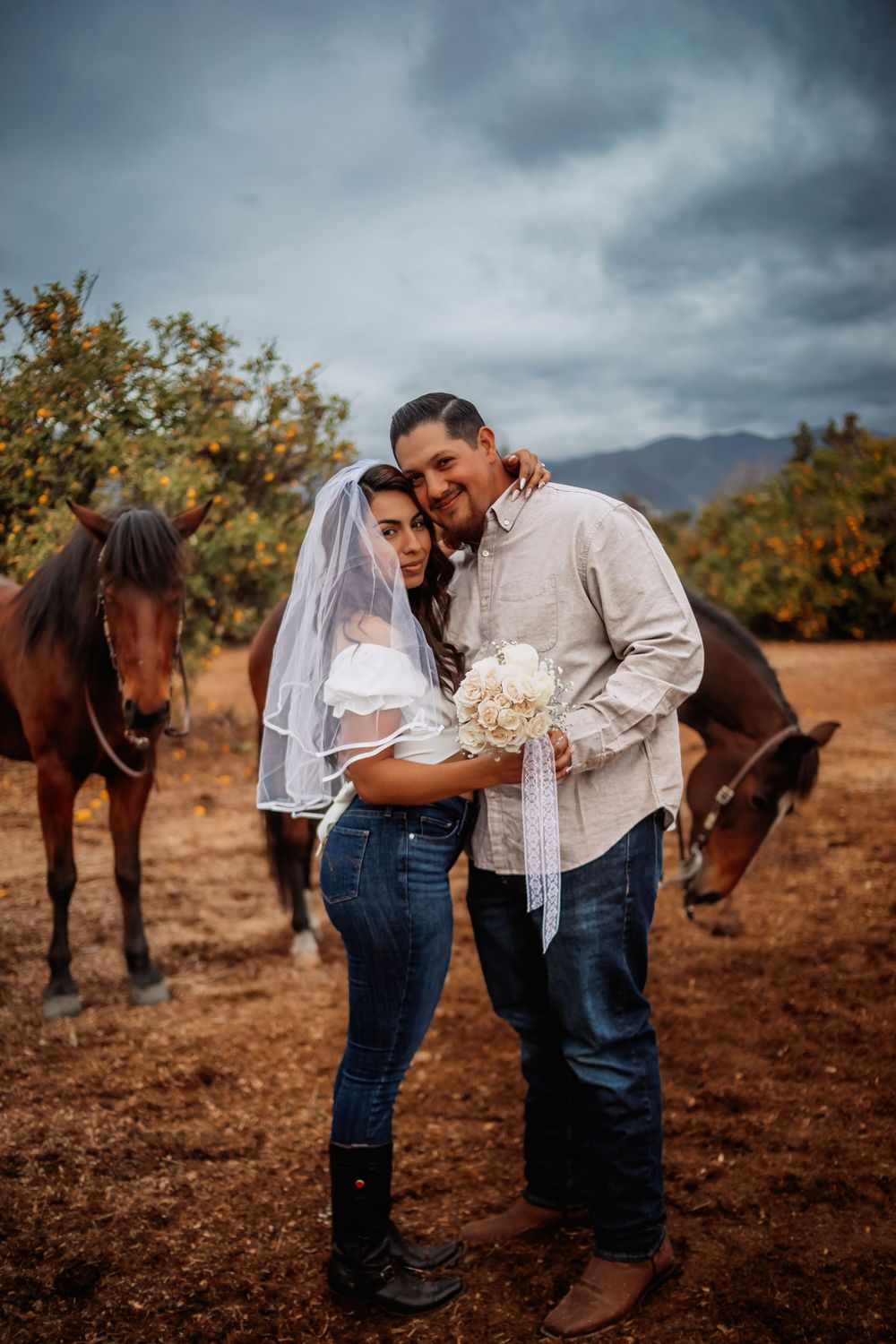 Cinematic romantic western engagement photography with a couple embracing in a field as horses graze in Norco California