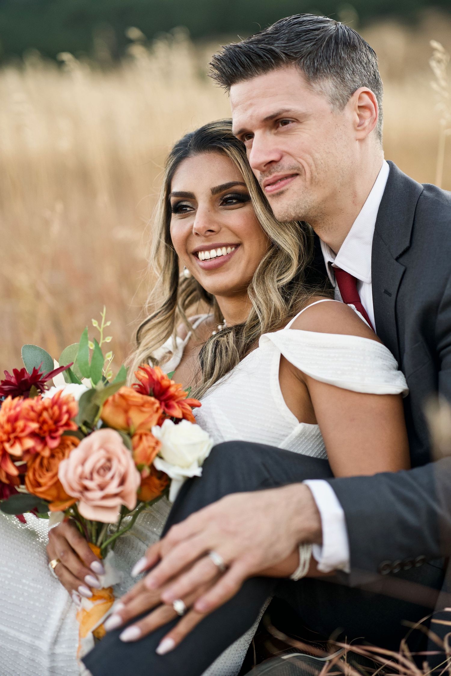 Wedding couple with autumn bouquet featuring orange and pink flowers in golden field.