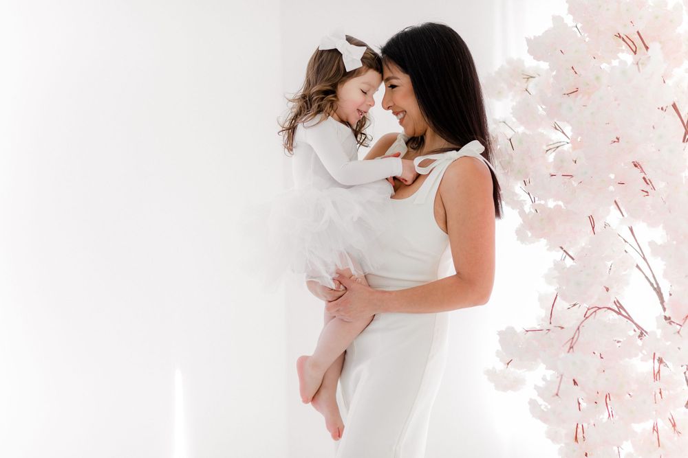 Ethereal white studio portrait with cherry blossom decorations creating a soft spring atmosphere.