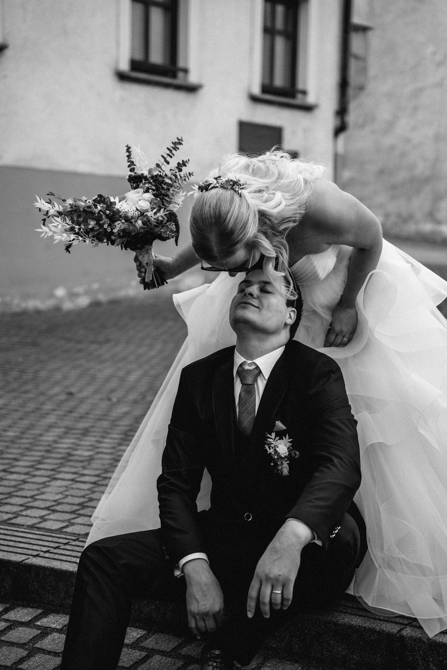 A black and white wedding portrait with artistic composition and floral bouquet.