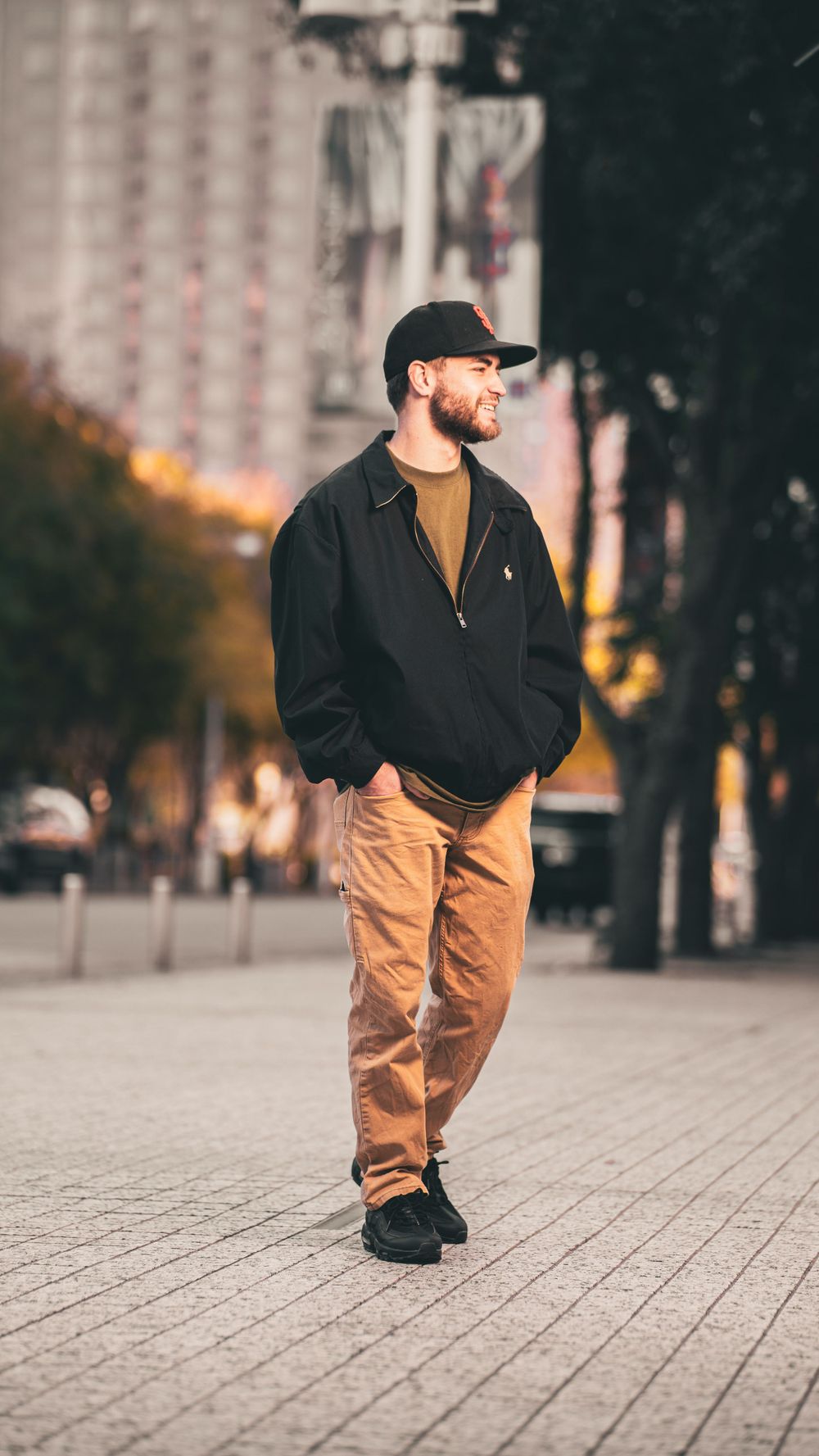 Casual street fashion portrait of someone walking in khakis and black jacket in an urban setting.