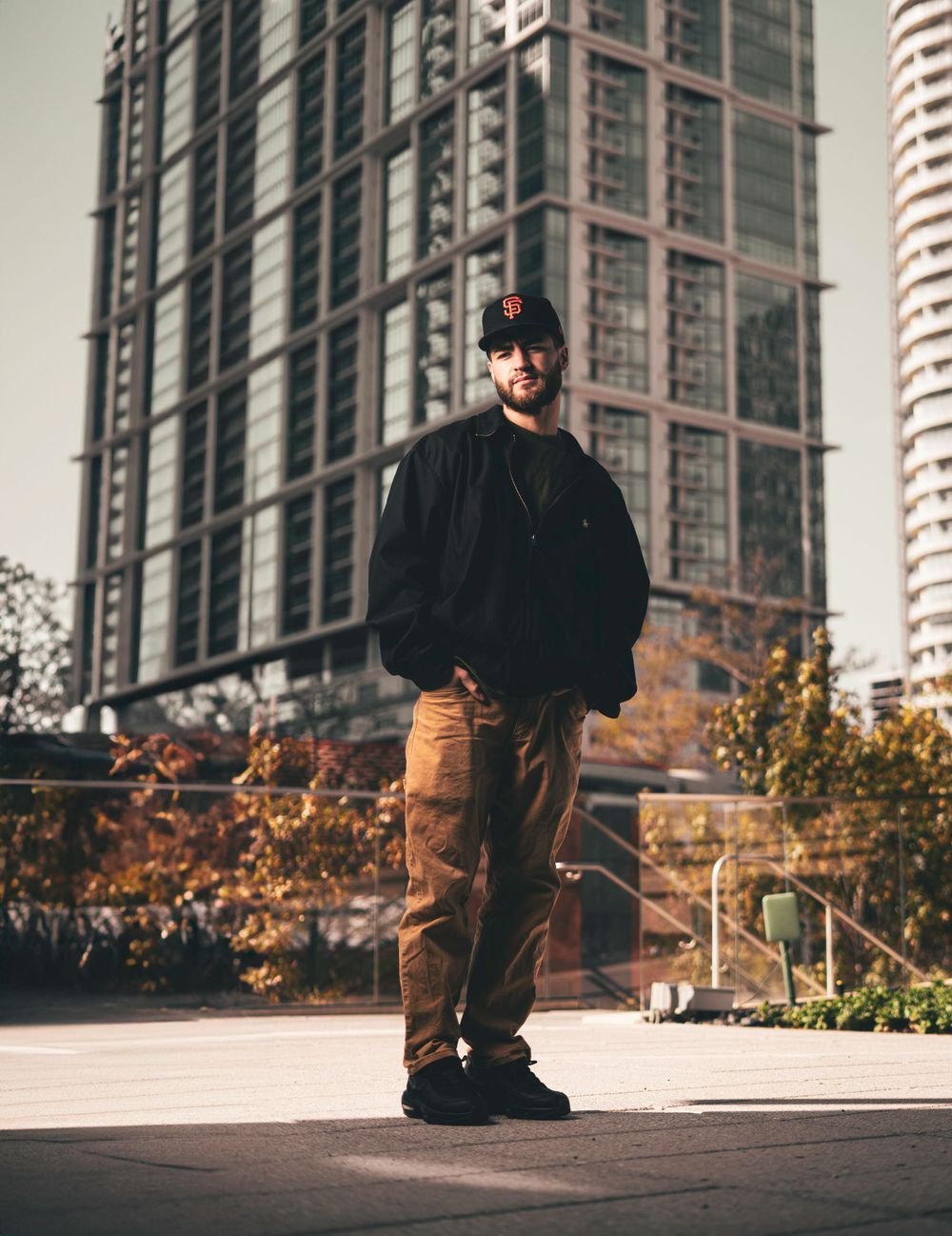 Casual street style portrait with urban architecture featuring someone in khakis and a black jacket.