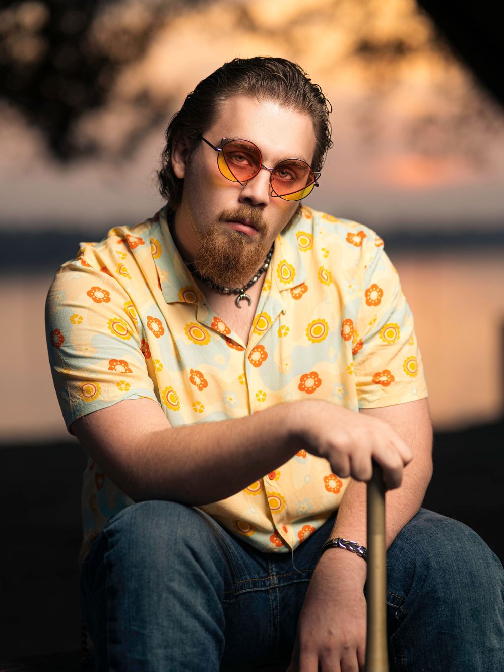 Portrait of person in yellow floral shirt sitting outdoors during sunset wearing orange-tinted glasses.