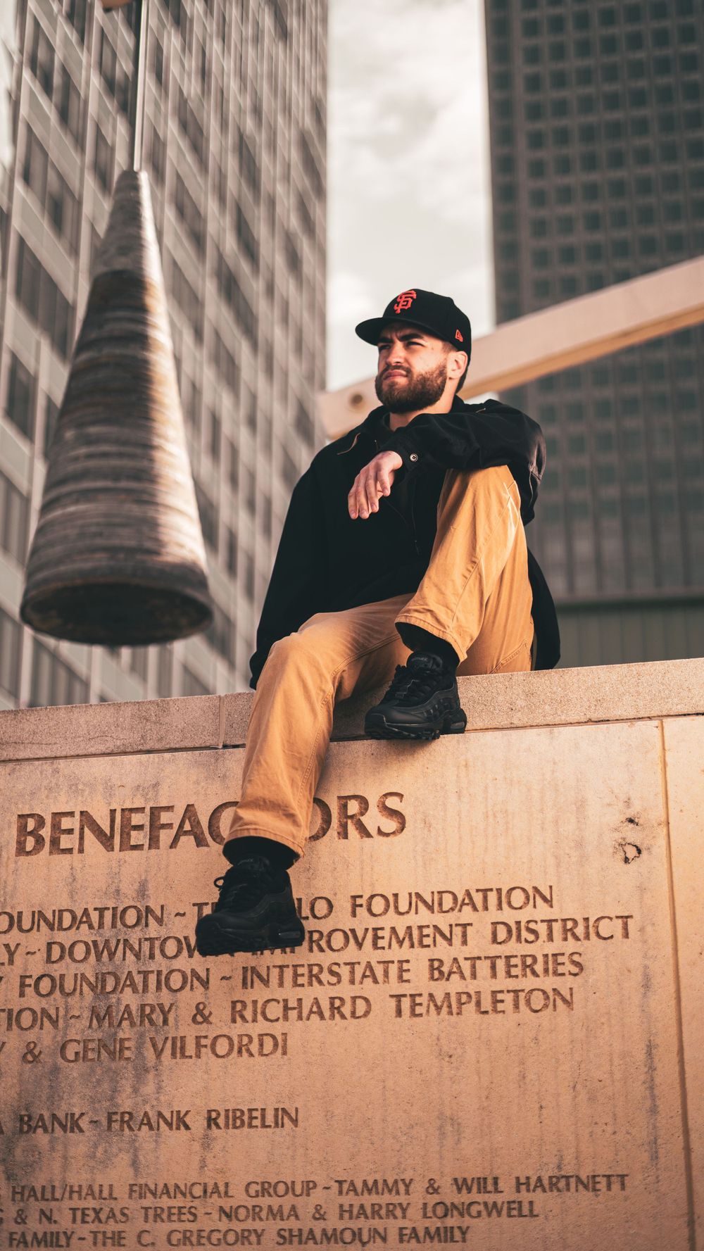 Urban photography of a person relaxing on a Benefactors monument with tall buildings in the background.