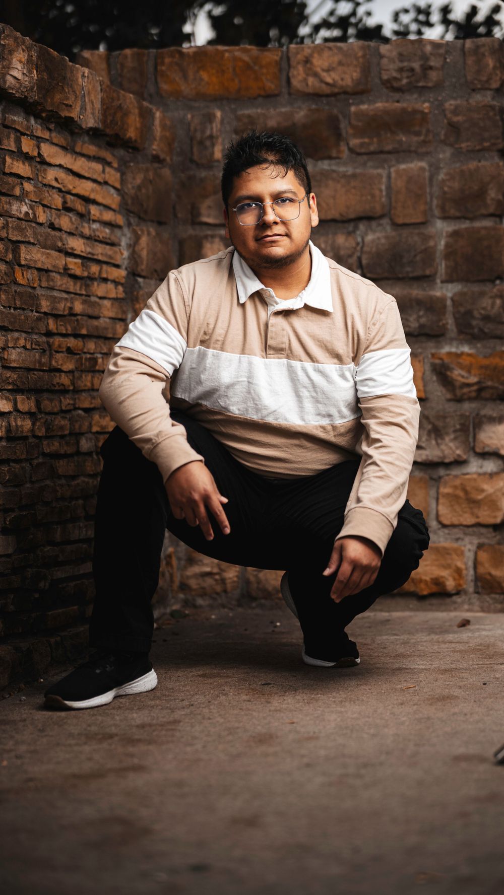 Portrait against brick wall wearing tan and white color block jacket and dark pants.